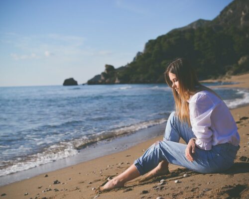 Girl setting on beach looking at the sand.